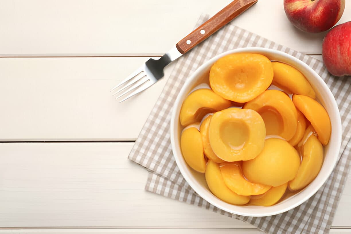 Bowl of canned peach halves with fresh peaches, representing canned fruit exports.