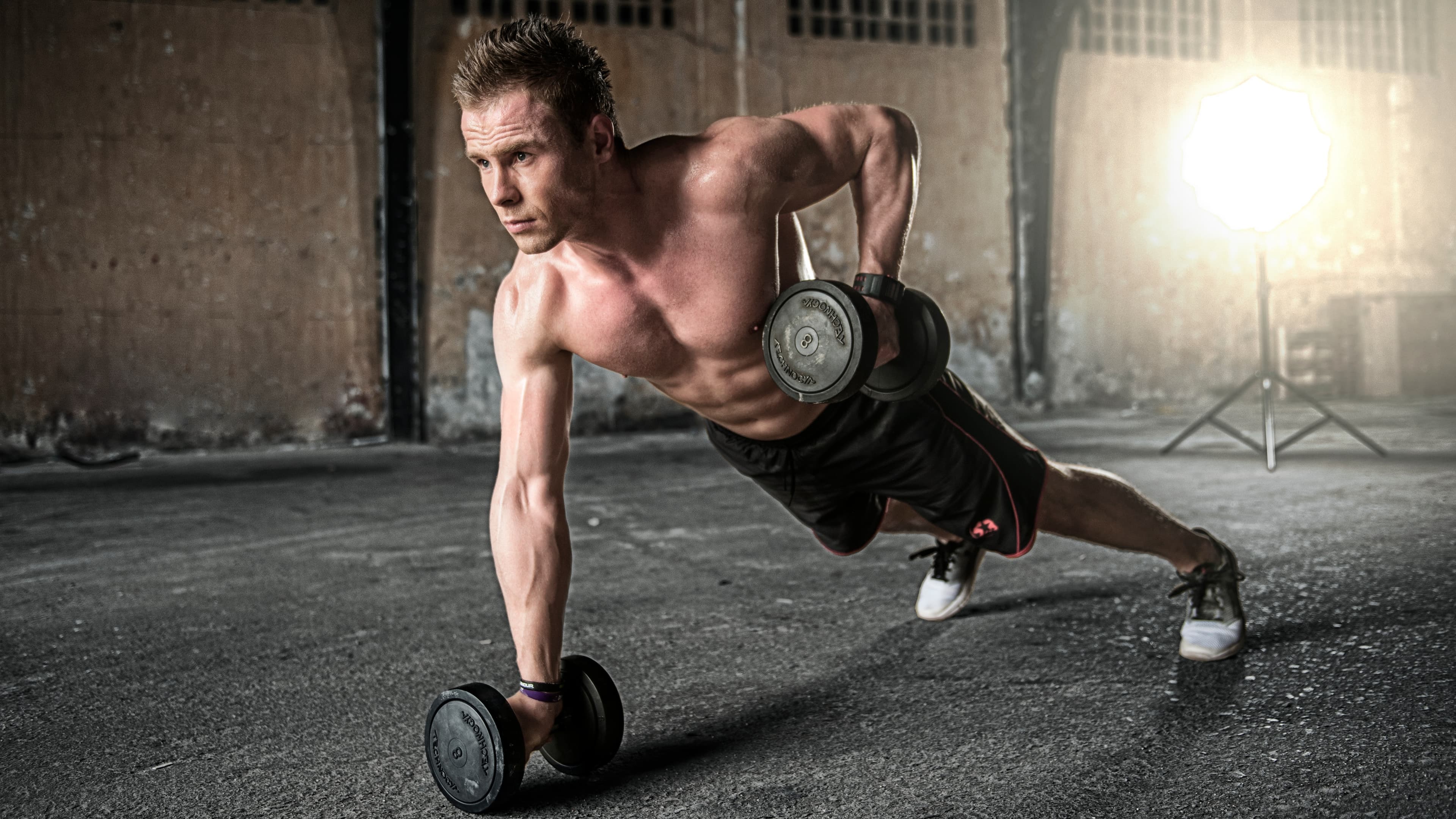 Athlete performing dumbbell rows in an industrial gym, symbolizing sports nutrition markets.